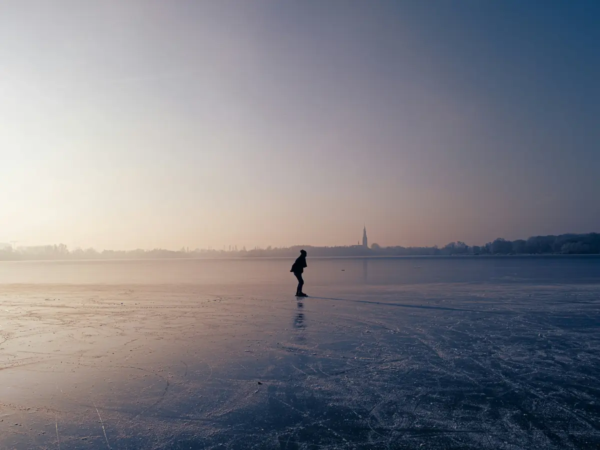 Un patineur seul au loin sur un lac gelé, au crépuscule.