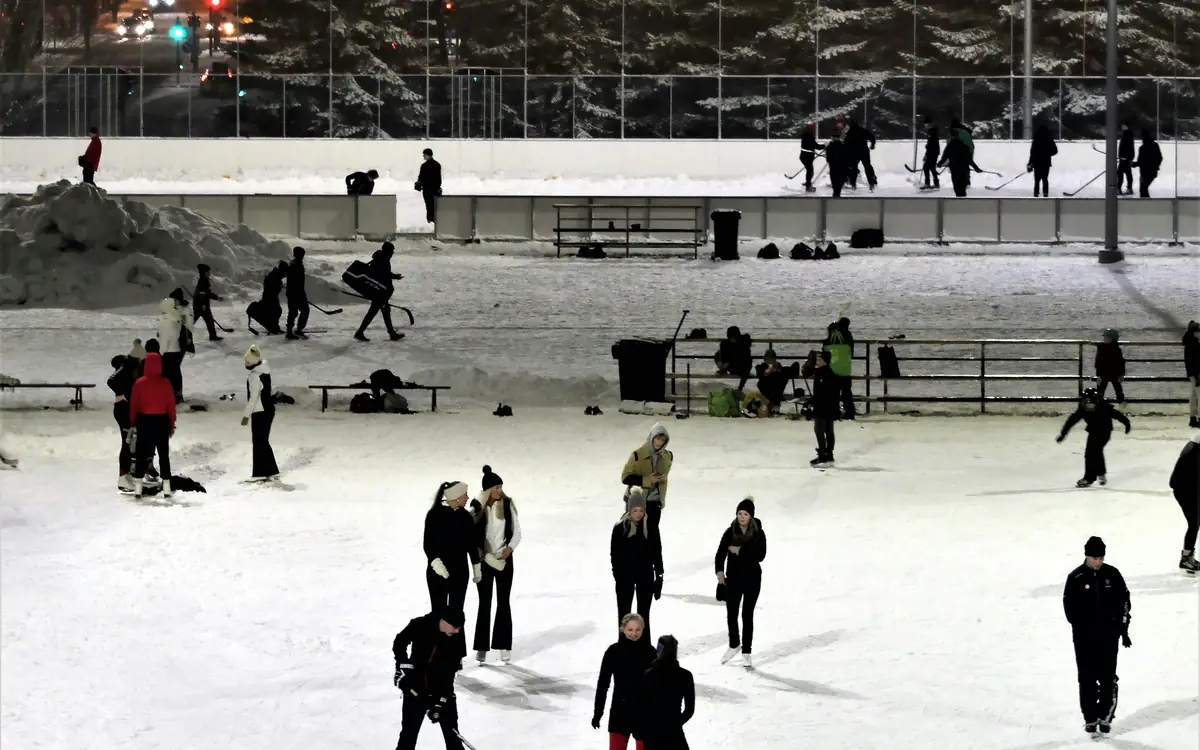 Patineurs et joueurs de hockey sur une patinoire extérieure éclairée, un soir d'hiver.